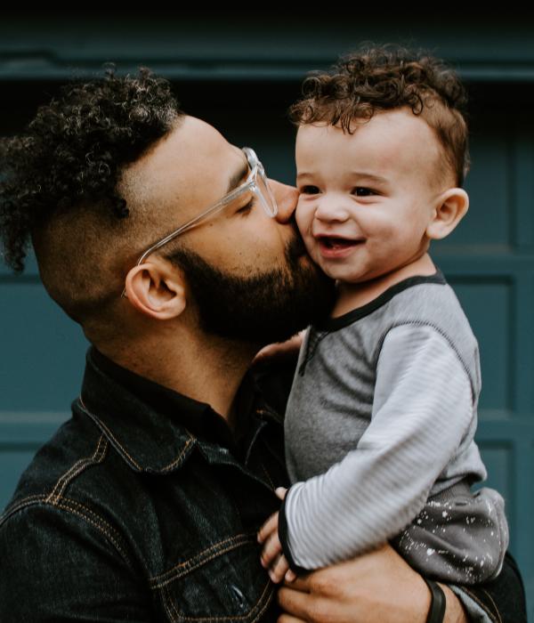 Adult holding a child up and giving them a kiss on the cheek.